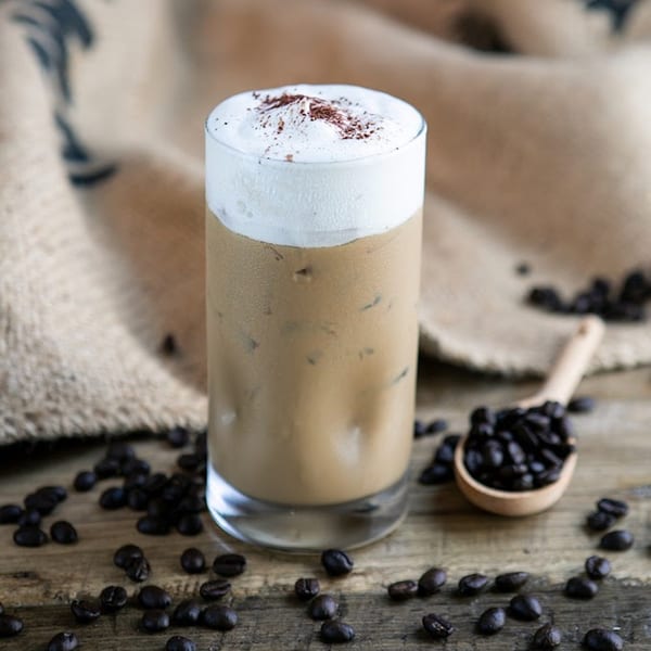 Iced coffee with whipped cream and coffee beans scattered on a rustic wooden surface.