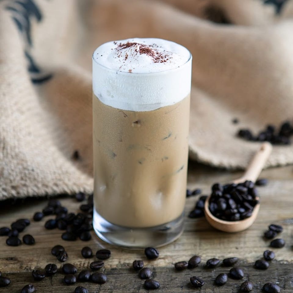 Iced coffee with whipped cream and coffee beans scattered on a rustic wooden surface.