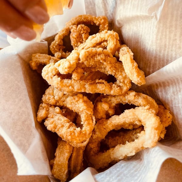Close-up of crispy fried calamari rings in a paper-lined basket, with a hand squeezing lemon.