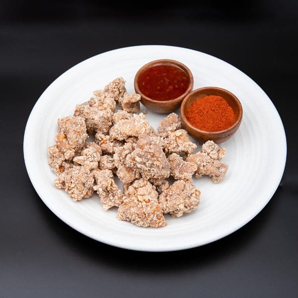 Hiccups' crispy popcorn chicken with sweet chili sauce and chili powder on a white plate.