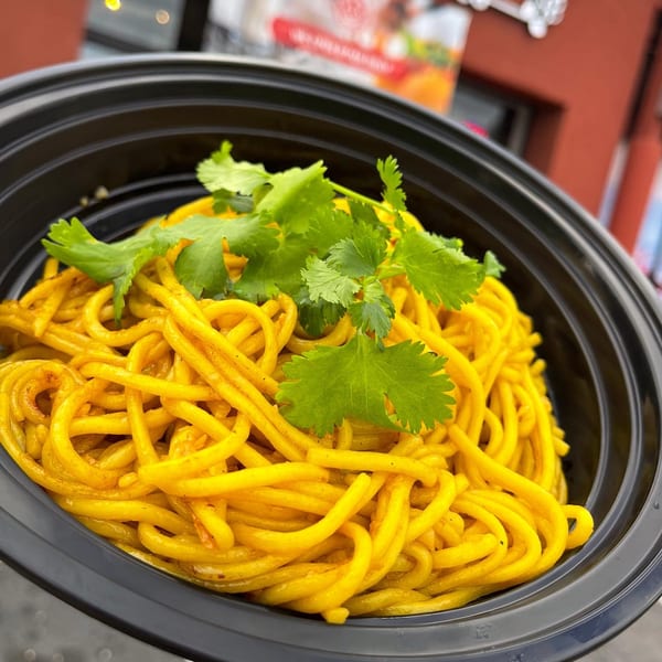 Hiccups' bright yellow noodles topped with fresh cilantro in a black takeout bowl.