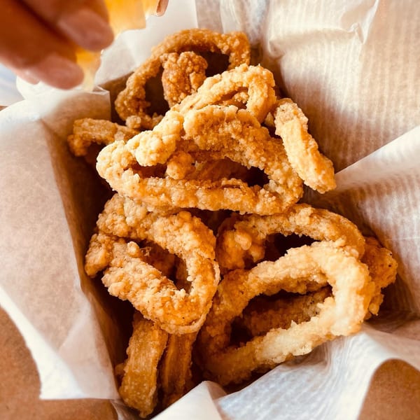 Crispy golden-brown fried calamari rings in a paper-lined basket, with a hand squeezing lemon over them.