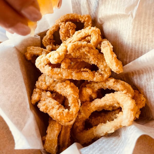 Crispy fried calamari rings in a paper-lined basket, with a hand squeezing lemon over them.