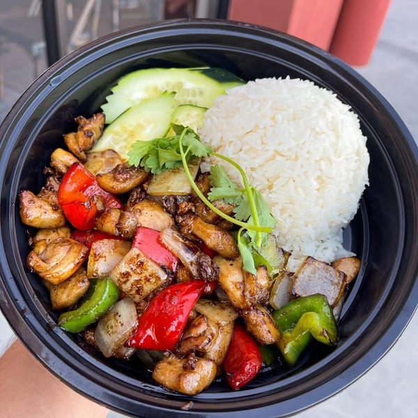 Hiccups' Asian-fusion dish with chicken, bell peppers, onions, rice, cucumbers, and cilantro in a black bowl.