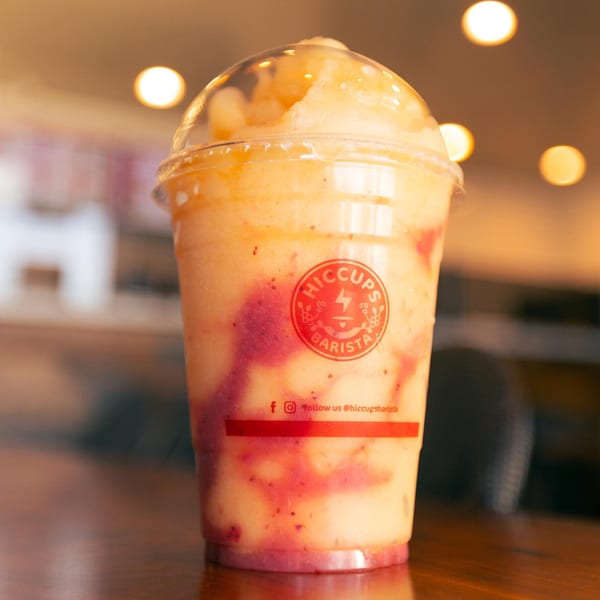 A Hiccups Barista fruit smoothie with red swirls in a clear cup on a wooden table.