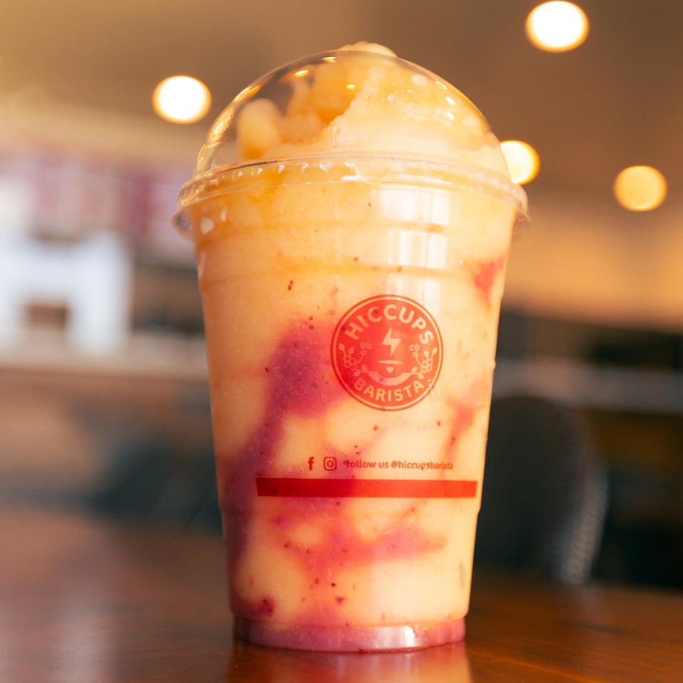 A Hiccups Barista fruit smoothie with red swirls in a clear cup on a wooden table.